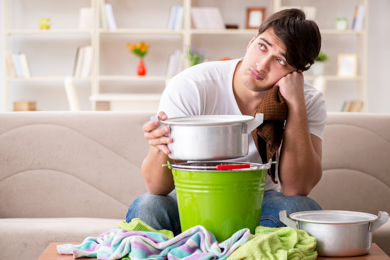 Man collecting water from leaking ceiling in need of home plumbing services